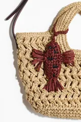 Cartera cruzada de paja trenzada de papel con doble asa, cierre magnético y correa bandolera ajustable. Incluye dije decorativo en forma de pez bordado en color bordó.