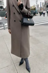 Bolso de mano mini estructurado en color negro, con asa superior fija y cierre frontal mediante clip metálico dorado. Incluye bandolera extraíble y bolsillo interior.