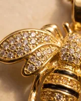 Collar de bronce dorado con cadena fina y un dije colgante en forma de abeja, adornado con circonias brillantes y detalles negros en el cuerpo.
