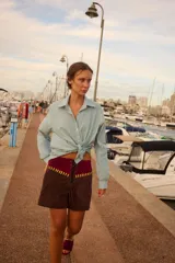 Shorts de cuero marrón con cintura alta de terciopelo burdeos, cordones frontales y apliques de cuero amarillo.