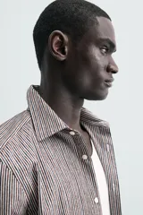 Camisa de corte regular fit confeccionada en algodón, con diseño de rayas verticales finas, cuello italiano, manga larga con puños abotonados y cierre frontal de botones.