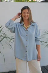 Camisa de jean en tono celeste claro, de corte holgado y diseño oversize. Presenta cuello clásico, cierre frontal con botones y mangas largas con puños con detalle de volado sutil.