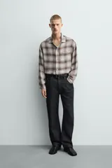 Camisa relaxed fit de manga larga con cuello solapa, confeccionada en tejido con mezcla de viscosa. Presenta un bolsillo plastrón en el pecho, bajo con aberturas laterales y cierre frontal de botonadura. El diseño es a cuadros en tonos beige y marrón.