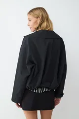 Campera corta de manga larga confeccionada en tejido técnico color negro. Presenta cuello solapa, cierre frontal con cremallera metálica y cinturón integrado con hebilla en la cintura.