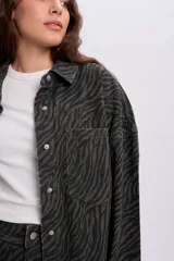 Sobrecamisa de denim con estampa de cebra en color verde militar, de corte oversize, cuello camisero, bolsillos frontales con solapa y cierre de botones metálicos.