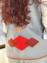 Chaleco gris de paño con bolsillos delanteros de tejido rústico color ladrillo y ribete color ocre. Diseño holgado.