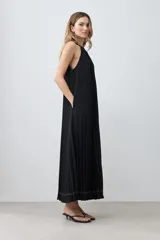 Vestido largo negro plisado con cuello halter y cinturón plateado.