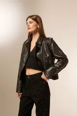 Chaqueta negra de cuero sintético con cuello solapa, cierre frontal asimétrico, bolsillos con cierre y tachas decorativas.