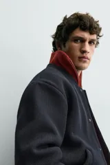 Chaqueta relaxed fit de color negro, confeccionada en tejido de canalé con mezcla de lana. Presenta cuello redondo, puños y dobladillo en rib elástico, bolsillos frontales de vivo y cierre con botones a presión.