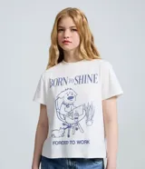 Remera de algodón color blanco con cuello redondo y mangas cortas. Presenta una estampa frontal en color azul con la frase 'Born to Shine' y una ilustración de un perro trabajando en una computadora.