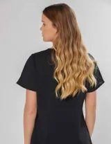 Blusa negra de manga corta con pequeños frunces en los hombros, escote redondo y abertura en la espalda con botón y pin metálico con logo.