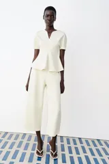 Top peplum confeccionado en hilatura de algodón de color bordó, con escote en V pronunciado, mangas cortas abullonadas y bajo con vuelo.
