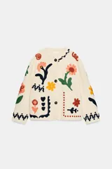 Chaqueta de algodón color crudo con cuello redondo, manga larga y bolsillos delanteros de plastrón. Presenta un diseño con bordados coloridos de flores y motivos abstractos a contraste, y cierre frontal con botones oscuros.