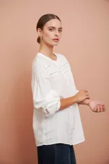 Camisa blanca de manga larga con escote redondo, puntillas y tablas al frente.