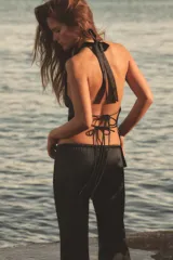 Top satinado de color beige con cuello halter drapeado, espalda descubierta y diseño de bajo asimétrico con terminación en punta y cordones colgantes. Cuenta con cierre de lazada en el cuello y la espalda.