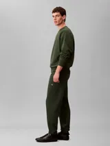 Pantalón jogger de felpa verde oscuro, con cintura elástica, bolsillos laterales y bajos ajustados en canalé. Incluye el monograma CK bordado en la pierna. Marca Calvin Klein.