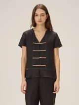 Camisa negra de manga corta, con cuello en V y cierre frontal de botones decorados con galones en zigzag de tono tostado.