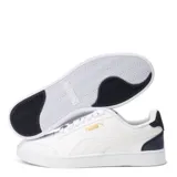 Championes Puma modelo Shuffle, de diseño urbano con silueta de bota baja. Presentan una parte superior de cuero sintético negro con la icónica franja lateral blanca y detalles en dorado. Incluyen perforaciones en la puntera para mayor ventilación y una suela de goma blanca.