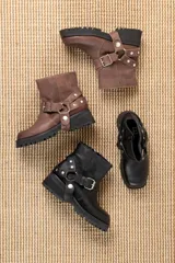 Bota corta de cuero negro con punta cuadrada, suela track y detalle de estribo desmontable con hebilla metálica.