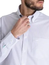 Camisa de manga larga RKF de corte regular fit, con diseño a rayas finas en tonos celestes y grises. Presenta cuello button-down, cierre frontal con botones, un bolsillo en el pecho con el logo bordado y detalles bordados en el puño.