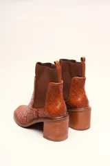 Bota tipo botineta de cuero negro con diseño trenzado artesanal en toda la capellada. Presenta paneles laterales elásticos, taco cuadrado de altura media y tirador en la parte superior trasera.