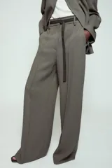 Pantalón de tiro alto con corte ancho y pernera recta. Presenta raya planchada en el delantero, bolsillos laterales y cierre frontal con cremallera y ganchos metálicos. Incluye un cinturón fino en tejido a contraste.