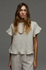 Blusa de lino color beige, de manga corta con volados, cuello redondo y espalda cruzada con volados.