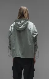 Campera rompevientos de diseño oversize, color verde, confeccionada en microfibra técnica ligera. Presenta capucha integrada, cierre frontal técnico y un sistema de frunces elásticos regulables a lo largo de las mangas que permiten ajustar el volumen de la prenda.