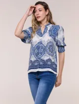 Blusa de crepe color blanco con estampado paisley en tonos azules y negros. Presenta cuello mao con escote en V, cierre frontal con botones y mangas cortas abullonadas con puños elastizados en punto smock.