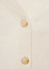 Cardigan de punto fino color crema, con cuello en pico, cierre frontal de botones y mangas largas con terminaciones en canalé.