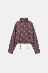 Cazadora marrón oscuro con estampado de lunares blancos, cuello subido, manga larga y bolsillos frontales. Cuenta con cierre frontal de cremallera y botones ocultos, y bajo ajustable con cordón.