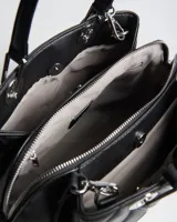 Cartera de símil cuero negro con diseño matelassé romboidal y tachas metálicas plateadas. Cuenta con dos asas de mano, correa bandolera regulable y desmontable, compartimento central con cierre y herrajes plateados con logo XL.