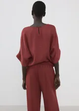 Blusa de diseño recto y color bordó, con cuello redondo, mangas tres cuartos y cierre de botón en la parte posterior del cuello.
