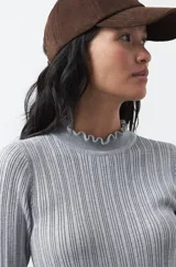 Polera de tejido acanalado color negro, con cuello alto y puños con terminación de volados. Presenta un diseño entallado y textura vertical.
