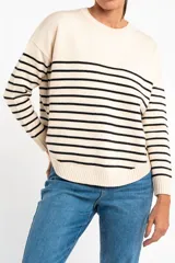 Sweater de punto con diseño a rayas horizontales negras sobre base color crema, cuello redondo, mangas largas y puños acanalados.