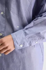 Camisa de silueta oversize de algodón color celeste, con cuello clásico, cierre frontal con botones, hombros caídos, bolsillo aplicado en el pecho y puños abotonados.