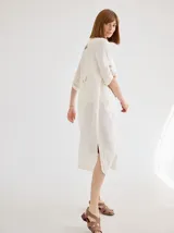 Vestido camisero midi de lino color beige, con diseño de manga corta con solapa, cuello camisero, bolsillo trasero con solapa y botón, y aberturas laterales en el ruedo.