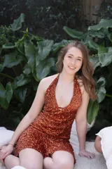 Vestido corto negro con escote en V profundo, estilo halter con tiras para atar al cuello. Presenta un diseño ajustado en el busto con tiras ajustables bajo el mismo que se cruzan y anudan en la espalda, y falda con volado en el ruedo con detalle de encaje.