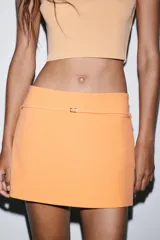 Falda pantalón de tiro medio color naranja, con diseño de corte recto y detalle de cinturón fino con hebilla metálica. Cuenta con cierre lateral oculto.