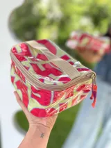 Neceser con estampado abstracto en tonos blanco, marrón y rosa. Tiene cierre superior con cremallera y asa de mano marrón.