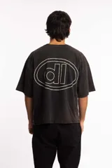 Remera de corte boxy fit, color negro con efecto lavado, de manga corta y cuello redondo. Presenta un logo bordado en el centro del pecho dentro de un óvalo.