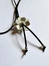Gargantilla con dije de flor plateada con centro de strass y cordón de gamuza negro con terminales plateadas.