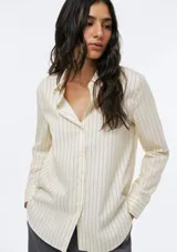 Camisa de corte clásico con cuello camisero, manga larga con puños vueltos y cierre frontal de botones. Presenta un diseño de rayas verticales finas en tono beige.