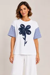 Remera blanca de algodón con mangas cortas a rayas azules y blancas, con aplique de flor en relieve de tela azul en el frente.