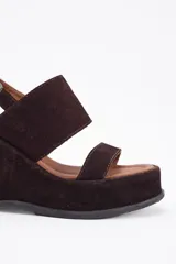 Sandalias de cuero vacuno color negro, con taco de cuña y tira ancha sobre el empeine. Ajuste con hebilla al tobillo.