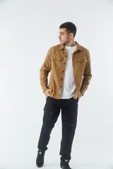 Sobrecamisa de jean color tostado, con cuello clásico, cierre frontal con botones y dos bolsillos frontales con solapa. Presenta mangas largas con puños abotonados y un pequeño parche decorativo en el ruedo.