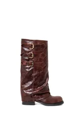 Botas de caña alta confeccionadas en cuero vacuno con acabado brillante. Presentan un diseño de caña holgada con tres correas horizontales ajustables mediante hebillas metálicas doradas. Cuentan con un taco bajo cuadrado y suela de goma resistente.