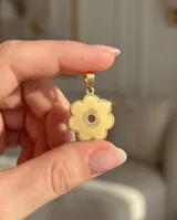 Dije con forma de flor de seis pétalos, con centro circular calado y detalle grabado, acabado en tono dorado.