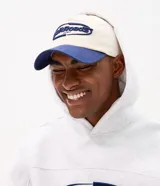 Gorra de béisbol con diseño bicolor, cuerpo en color crema y visera en azul marino. Presenta un bordado frontal con lettering en relieve color azul.