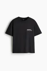 Remera negra de algodón con cuello redondo acanalado y mangas cortas de hombros caídos. Presenta un pequeño estampado tipográfico en el pecho con las palabras "No Defeat Just Glory".